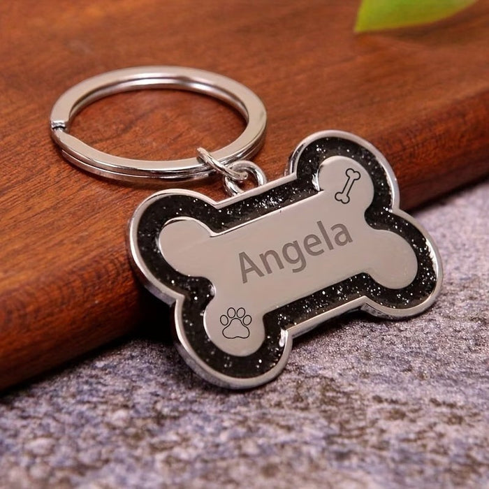 Blessing Sells silver bone-shaped pet ID tag with black glitter border and engraved name 'Angela', paw print, and bone icon.