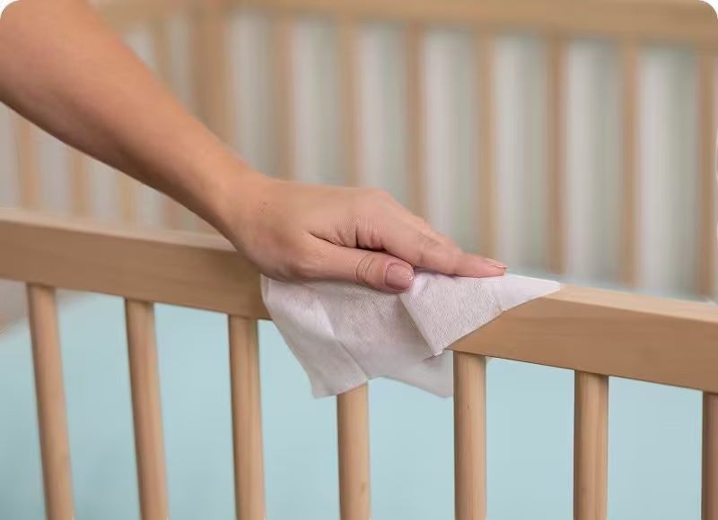 Blessing Sells hand cleaning wooden crib rail with Pampers Complete Clean wipes.